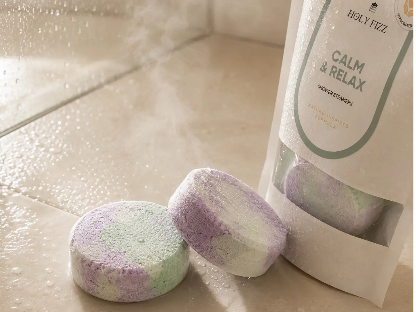 ก้อนอโรม่าสำหรับใช้ในห้องอาบน้ำกลิ่น Calm and Relax สีพาสเทล วางข้างบรรจุภัณฑ์บนพื้นห้องอาบน้ำที่เปียก