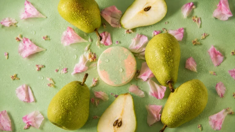 Holy Fizz Fleur de Pear green and peach shower steamer surrounded by fresh green pears and pink flower petals on mint green background