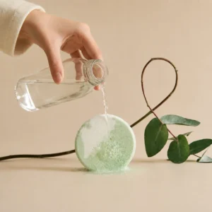 Holy Fizz Eucalyptus Boost Shower Steamer fizzing with water poured from glass bottle eucalyptus branch home spa how to use