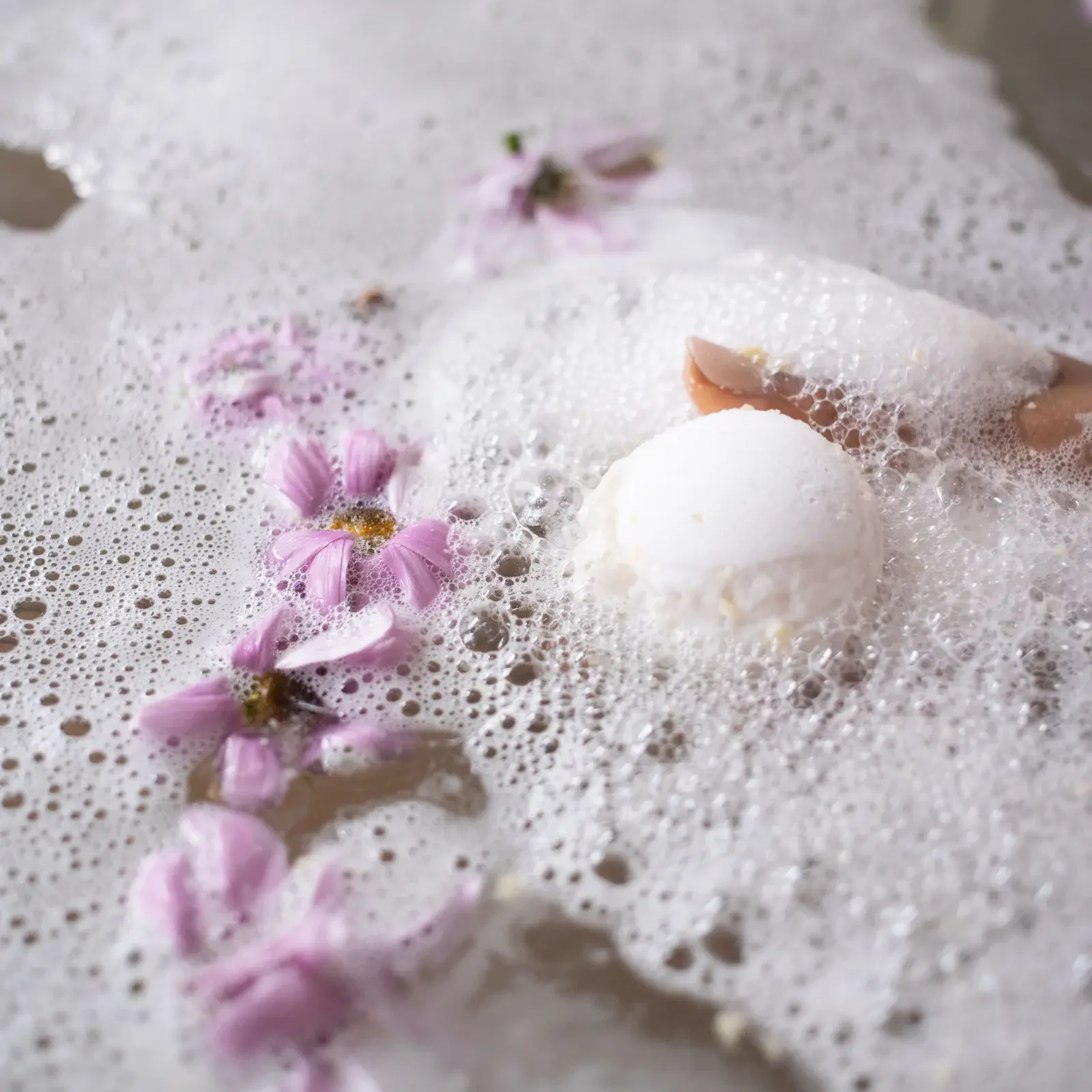 White bath bomb dissolving in foamy water with delicate pink flowers