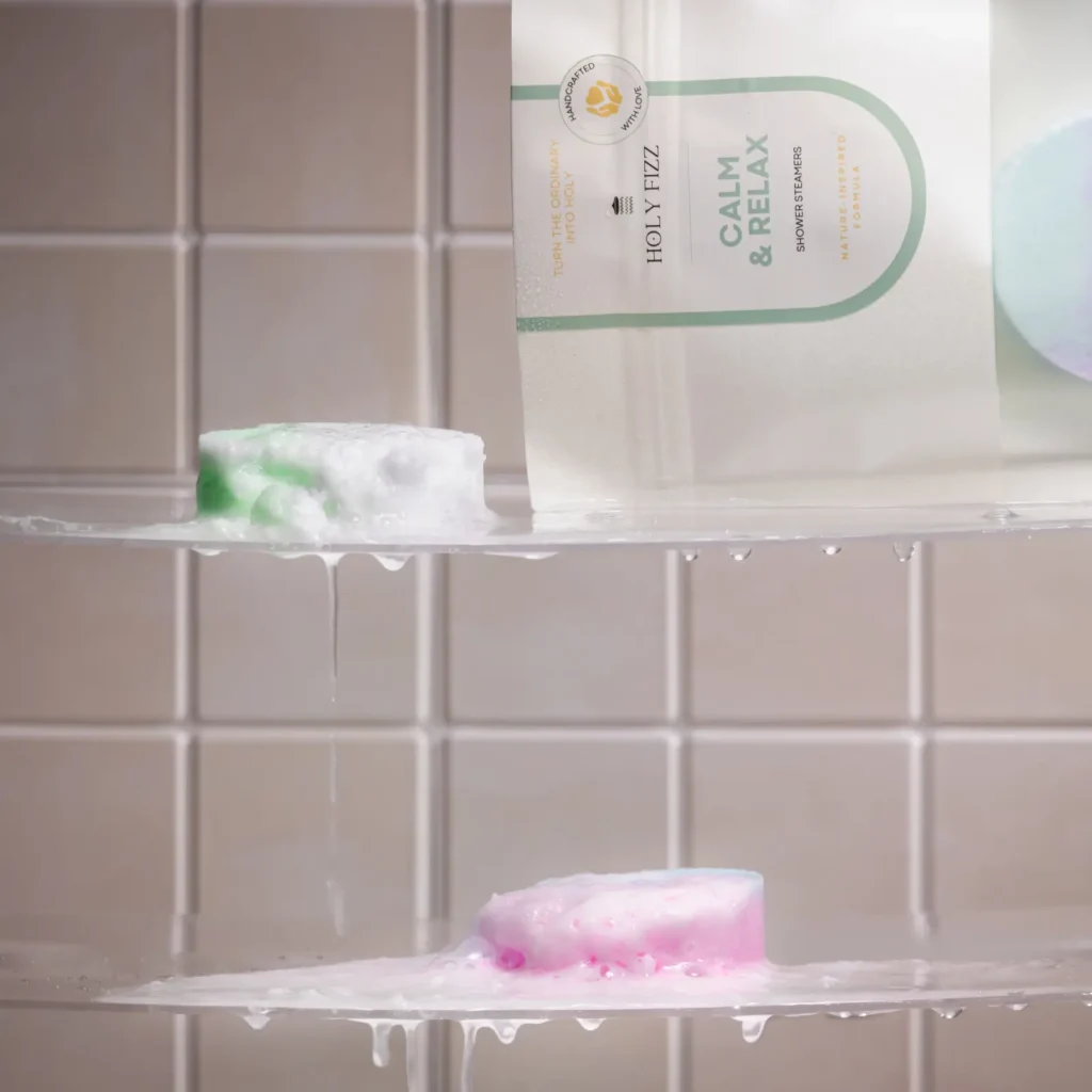 Holy Fizz Calm & Relax shower steamers on a wet shower shelf with colorful steamers dissolving in water