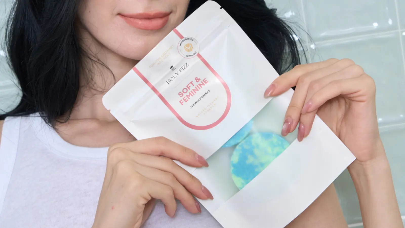 ผู้หญิงถือ Holy Fizz Soft & Feminine Shower Steamers พร้อมชาวเวอร์สตีมเมอร์สีฟ้าและเขียว